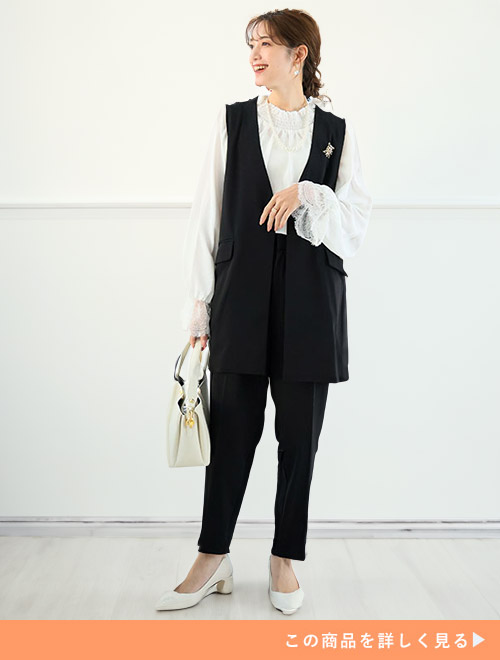 ホワイトフリルブラウスにジレとパンツのブラックセットアップスーツを合わせる女性