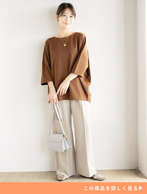 ブラウンのポンチトップスとホワイトのセンタープレスパンツのコーデにホワイトバッグを持つ女性