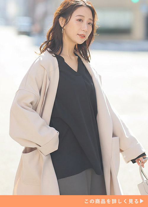 黒のVネックブラウスを着て、ベージュのアウターを羽織る女性
