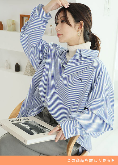 アイボリーのハイネック×ストライプ柄シャツを着て、グレーのボトムを履く女性