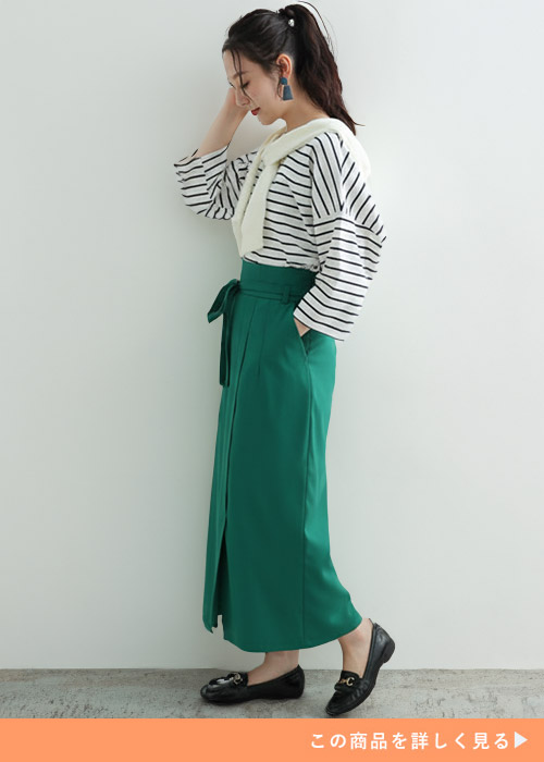 白黒ボーダートップスに白トップスを肩掛けし、グリーンのタイトスカートを履く女性
