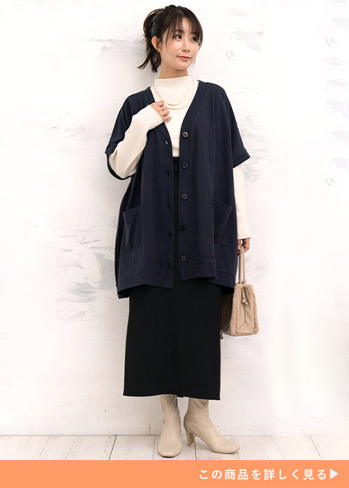 白のタートルニット×黒のタイトスカートを着て、黒のニットベストを羽織る女性