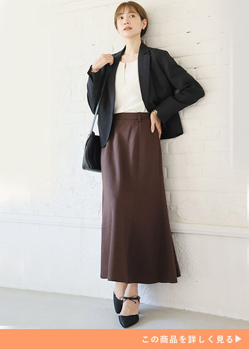 白系トップス×ブラウンのマーメイドスカートを着て、黒のジャケットを羽織る女性