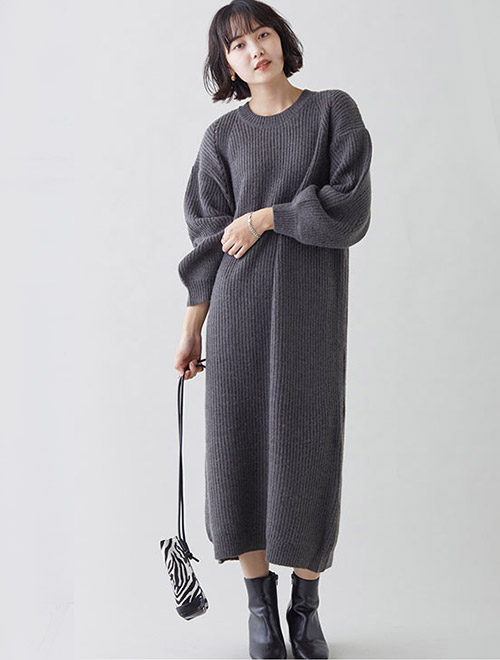 グレーのロングニットワンピースを着て、黒のショートブーツを履く女性