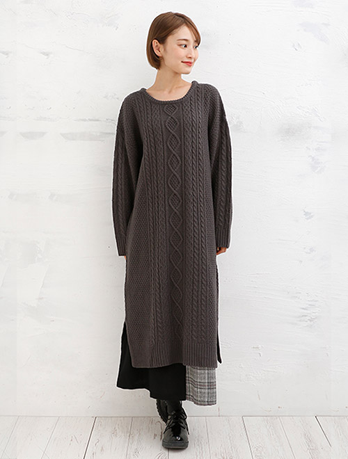 濃いグレーのケーブルニットワンピースを着に、チェック柄スカートを合わせた女性
