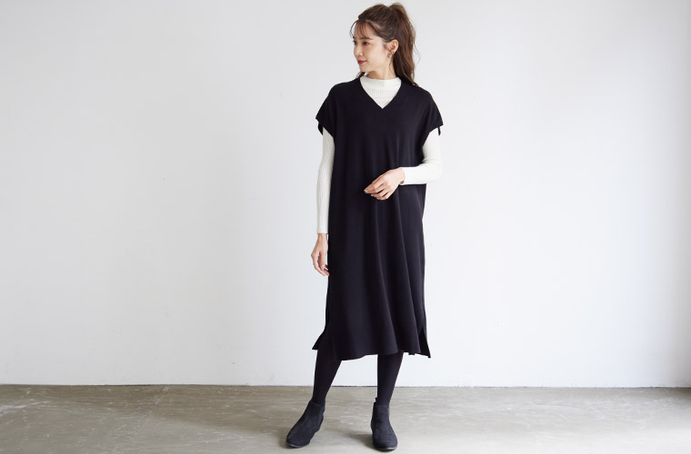 白のハイネックトップスに黒のベストデザインのニットワンピースを合わせた女性