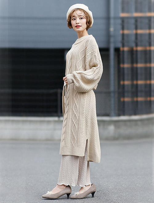 白のケーブル素材のニットワンピースを着て、同系色のパンツを合わせた女性