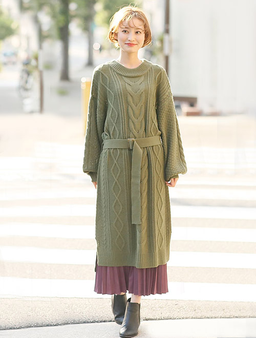 カーキのロングニットワンピースに、パープルのプリーツスカートをレイヤードした女性