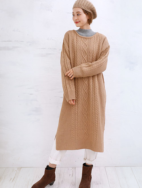 ニットワンピースピに、グレーのハイネックトップスと白のパンツをレイヤードした女性