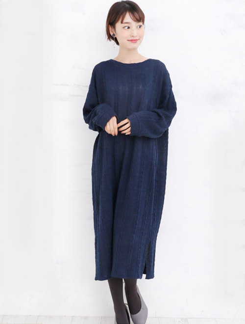 ネイビーのロングニットワンピースを着て、グレーのパンプスを履く女性