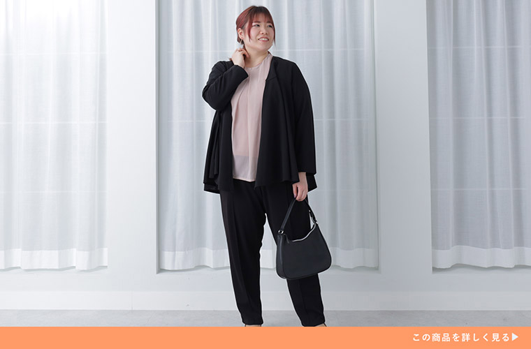 くすみピンクのシアートップスに、黒のジャケット×テーパードパンツを着る女性