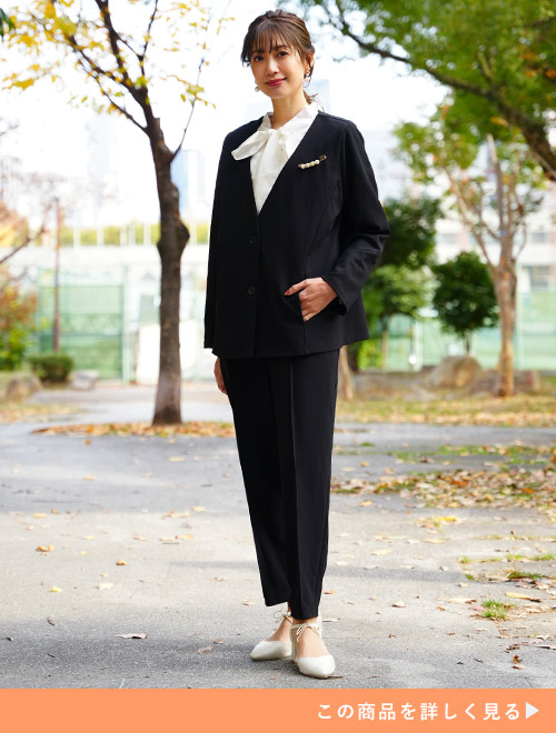 白色のブラウスに黒のセットアップスーツを着る女性