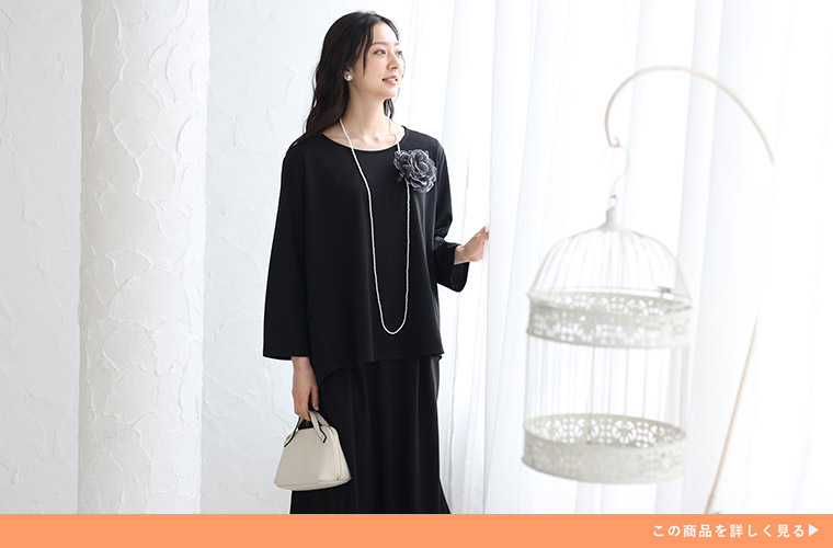 黒色のブラウス×スカートを着て、コサージュやロングネックレスをつける女性。