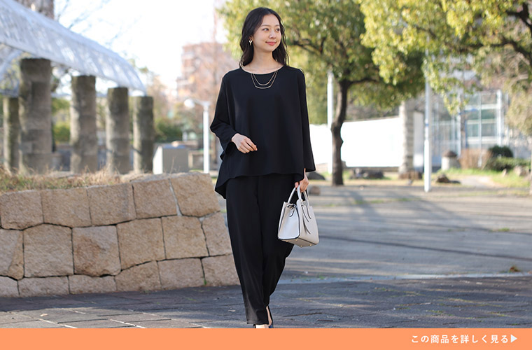 黒色のテーパードパンツ×バックフリルのブラウスを着る女性