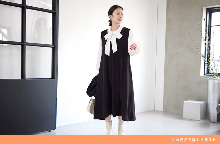 白色のリボンタイブラウスに黒色のジャンパースカートを着る女性