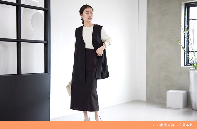 白のトップスに、黒色のジレ×ナロースカートのセットアップを着る女性