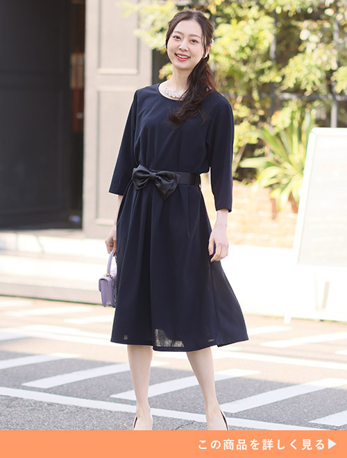 大ぶりなリボンベルトが付いた黒色の膝丈ワンピースを着る女性