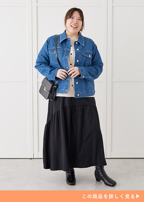 ドット柄のトップスを着て、黒のスカートを履き、デニムジャケットを着た女性