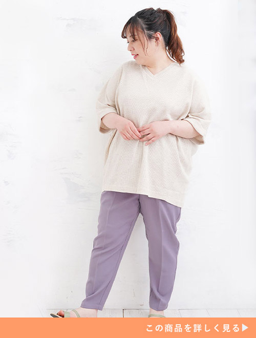 杢（もく）ベージュ色のVネックプルオーバーを着て、くすみ紫のパンツを履く女性。