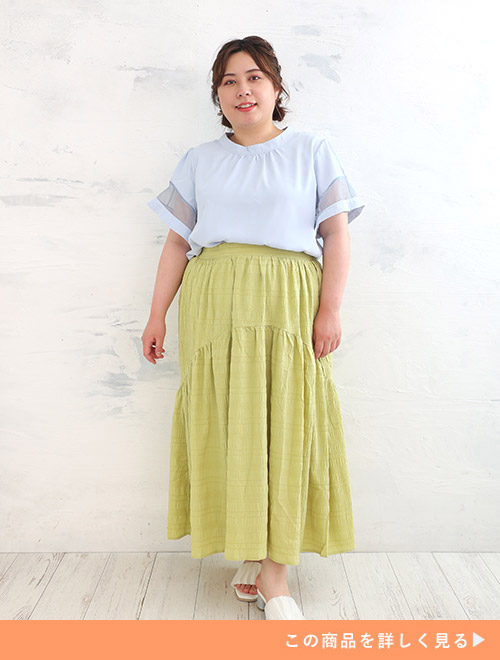 袖に透け感のあるサックスブルーのトップスを着て、黄緑色のロングスカートを履く女性