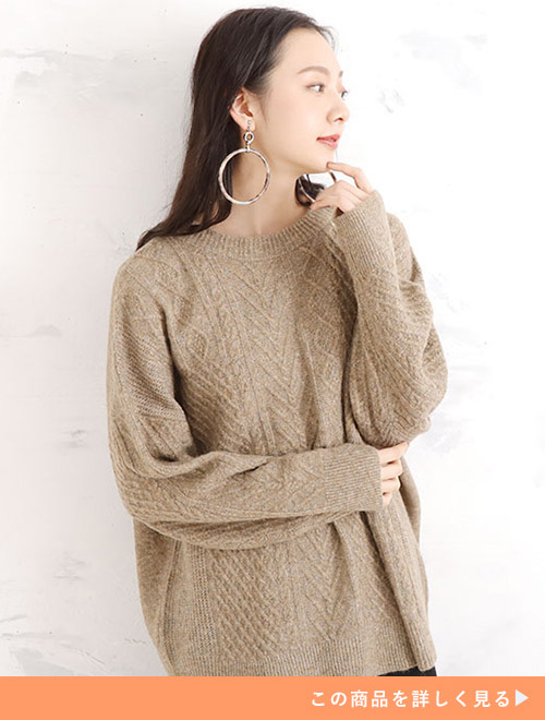 モカ色のケーブル編みニットをゆったりと着て、黒のボトムを履く女性