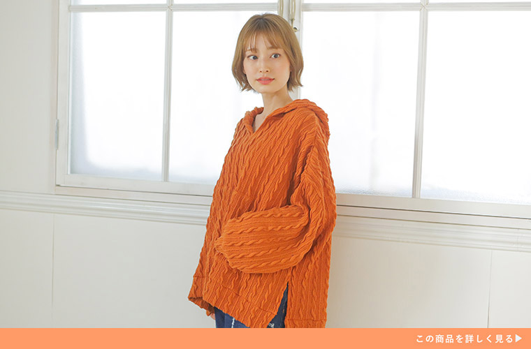 オレンジ色のケーブル柄ニットソーのパーカーを着て、デニムのボトムを履く女性