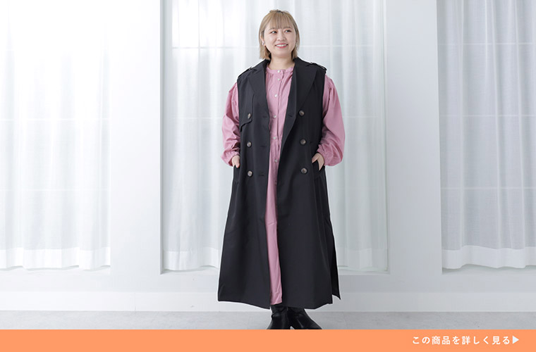 ピンク色のロング丈ワンピースに、黒のノースリーブトレンチコートを羽織る女性