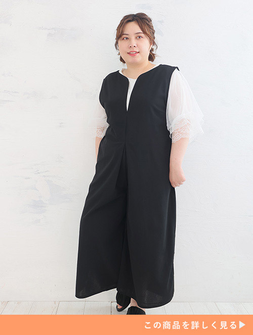 シアー袖の白トップスに深Vネックの黒オールインワンを重ね着する女性