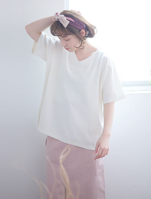 オフホワイトのVネックTシャツを着て、淡いピンクのボトムを履く女性