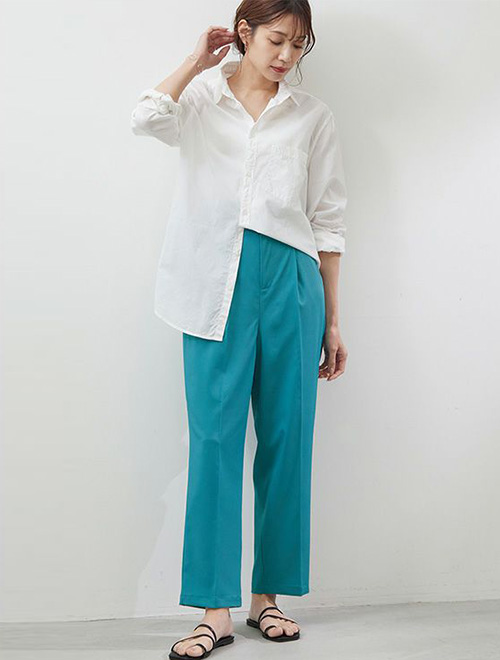 ピーコックグリーンのパンツに、白シャツの裾を片方だけインして着る女性