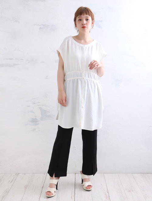 ギャザーが入ったオフホワイトのチュニックブラウスを着て、黒の裾スリットパンツを履く女性