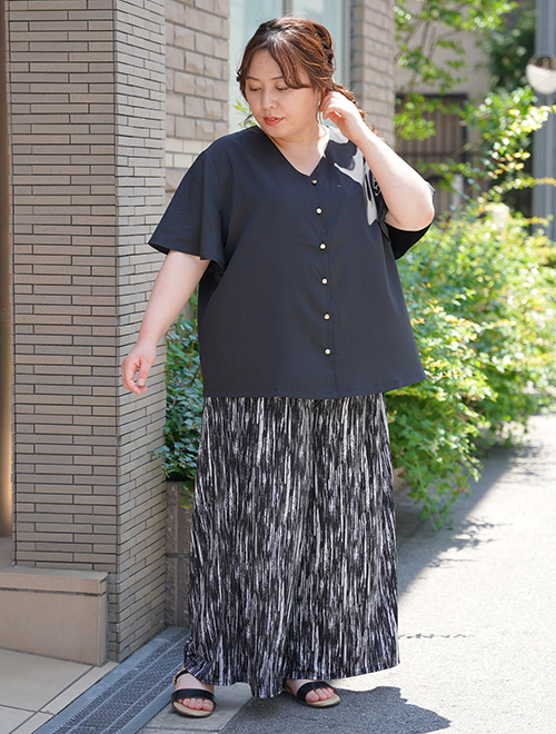 とろみ素材の黒のVネックブラウスを着て、モノトーンの柄ワイドパンツを履く女性