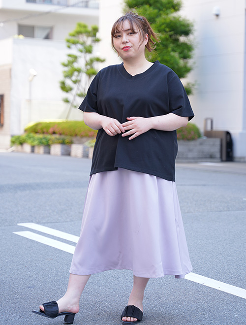 黒のVネックTシャツを着て、淡いパープルのミモレ丈スカートを履く女性