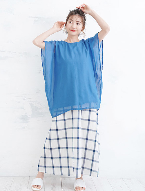 ダスティーブルーのシフォン重ねトップスを着て、白地に青の格子柄スカートを履く女性。