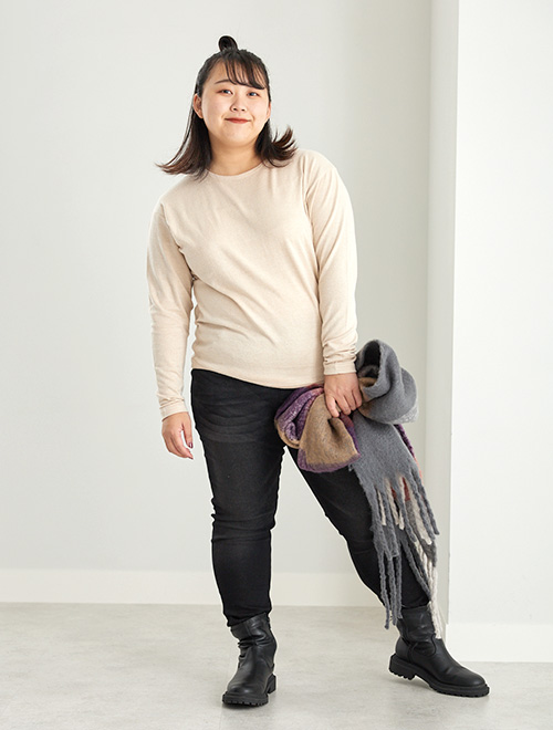 オフベージュのUネックニットソー×黒スキニーパンツを履く女性。手にはマフラーを持っています
