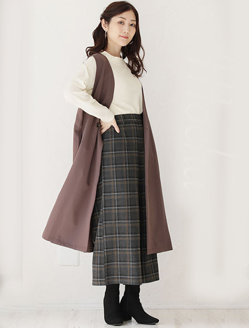 オフホワイトトップス×チェック柄マキシ丈スカートに、モカ色のロング丈ジレを羽織る女性