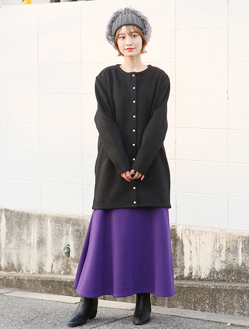 黒のスナップボタンカーディガンを着て、パープルのスカートを履く女性