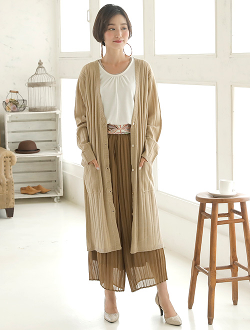 白トップスとブラウンのプリーツパンツのコーデに、ベージュのリブカーディガンを羽織った女性