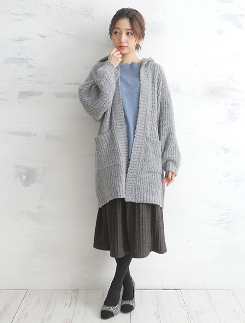 ブルーのトップスと黒のスカートのコーデに、グレーのロングカーディガンを羽織った女性