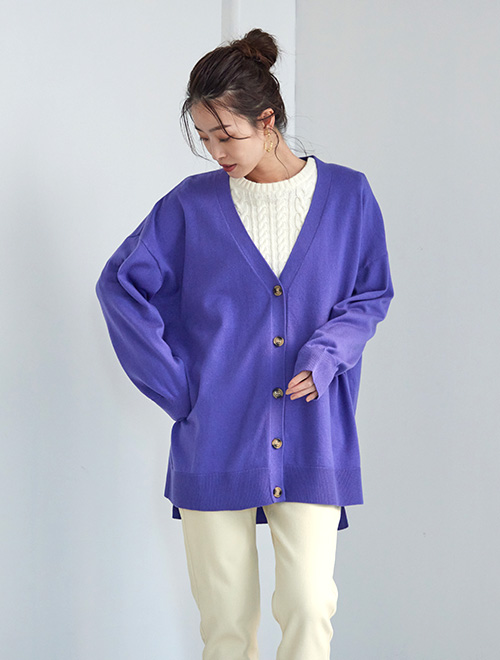 白のケーブルニットの上から、パープルのカーディガンを羽織り、白のパンツを履く女性