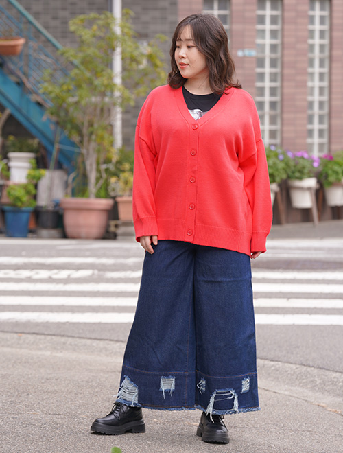 ピンクのカーディガンを着て、ダメージデニムパンツを履く女性