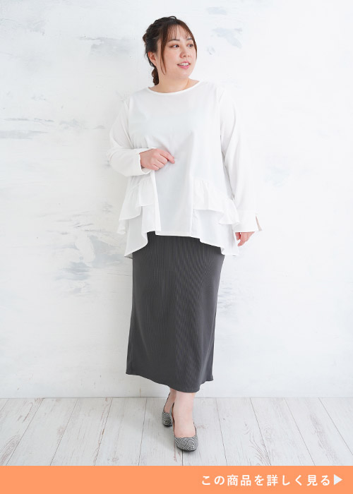 白のフリルチュニックを着て、グレーのタイトスカートを履く女性