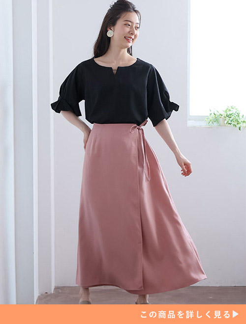 ピンク色のマキシ丈ラップスカートに、黒ブラウスをトップスインして着る女性