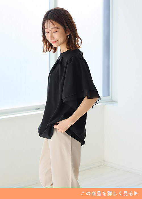 黒のとろみ素材ブラウス着て、ベージュのパンツを履く女性