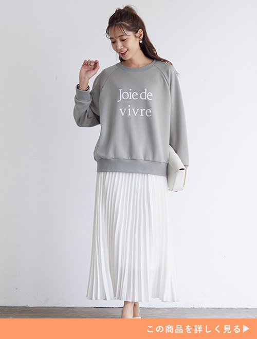 グレーのロゴトップス×白のマキシ丈プリーツスカートを着る女性