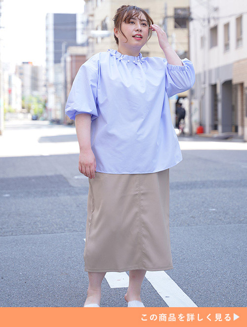 サックス色のブラウスを着て、ベージュのタイトスカートを履く女性。