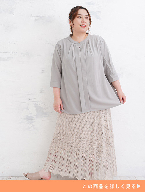 グレーのバンドカラーブラウスに、同系色のレース編みスカートを合わせて着る女性