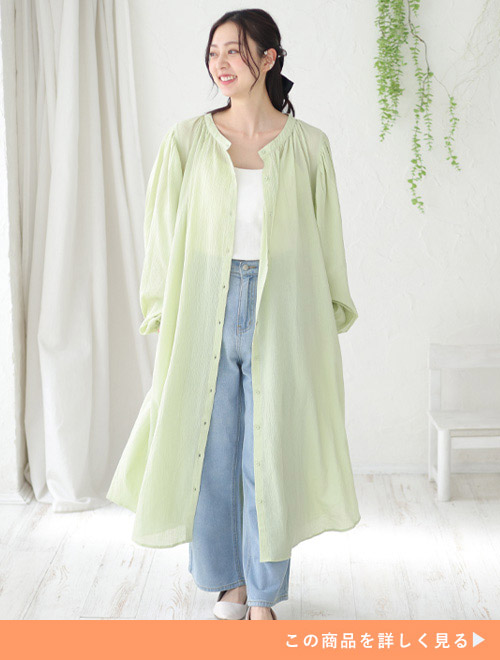 白のキャミソール×薄色デニムパンツに、ボタンを開けたライム色の透け素材シャツワンピースを羽織る女性