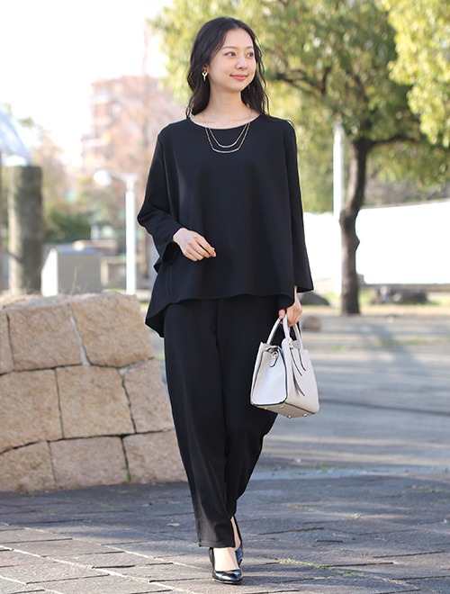 黒のブラウスとテーパードパンツのセットアップを着た女性