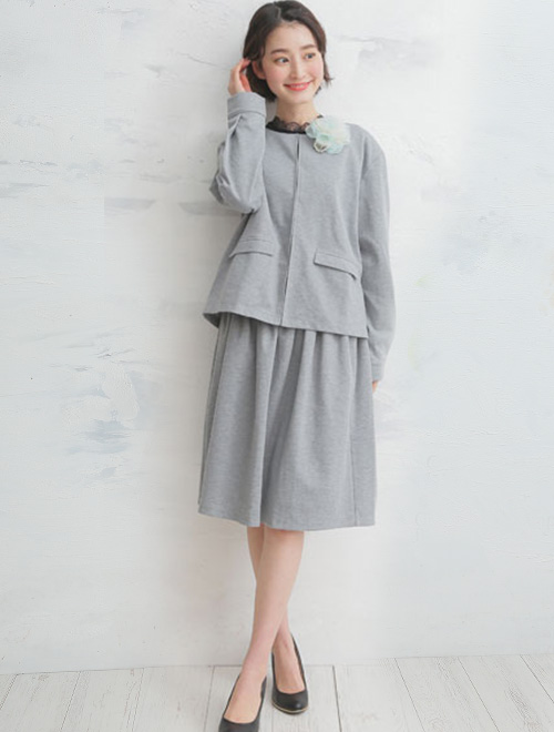 グレーのノーカラージャケットと、ギャザースカートのセットアップを着た女性